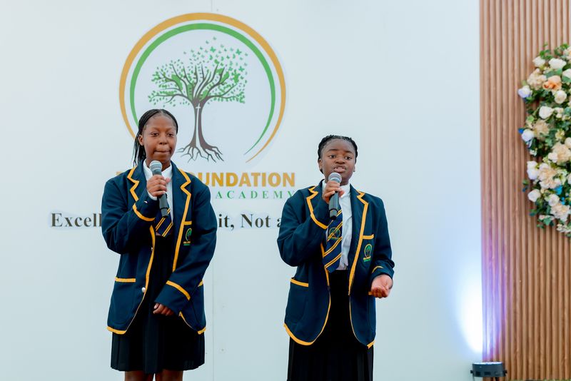Uniformed learners performing in front of the Firm Foundation school logo